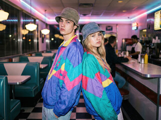 Retro 90s Style Couple Wearing Colorful Windbreakers and Bucket Hats in Vintage Diner