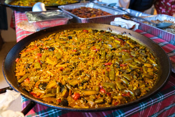 Traditional Valencian paella with chicken and vegetables served in a large pan at a family gathering, spacious background with blurred details
