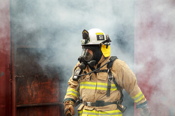 Obraz premium Firefighter in full gear emerging from a smoke filled or burning structure.