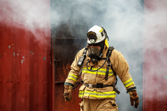 Firefighter in full gear emerging from a smoke filled or burning structure.