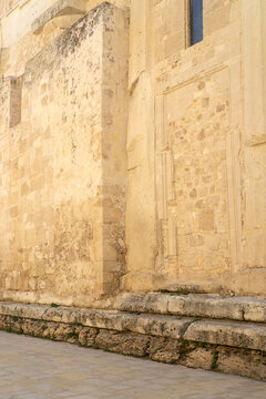 detailed photograph showcasing the ancient stone exterior of the Cathedral of Syracuse (Cattedrale di Siracusa) in Sicily. The image highlights the weathered limestone walls, historic architectural