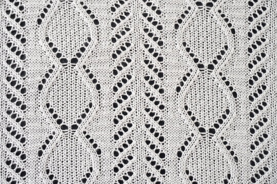 Detailed close-up of a lace knitting pattern, characterized by its repeating diamond-shaped motifs with openwork sections. Lace knitting is achieved by creating holes using yarn overs and decreases.