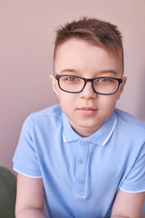 Fototapeta premium Caucasian male child with glasses in blue polo shirt posing calmly indoors.
