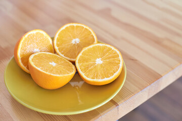 Fresh orange halves on yellow plate resting on wooden table surface in bright natural light.
