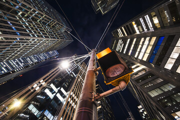 Fototapeta premium Nighttime upward view of towering glass buildings converging above a glowing traffic light, creating a dynamic sense of motion
