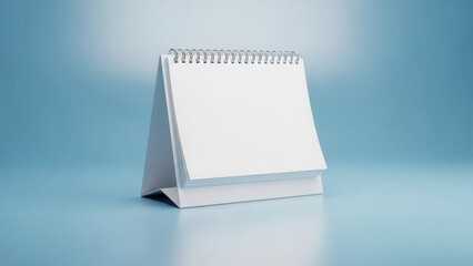 Blank desk calendar with white pages standing on a reflective surface against a blue background