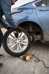 A man changes the wheel on a blue car with a wrench