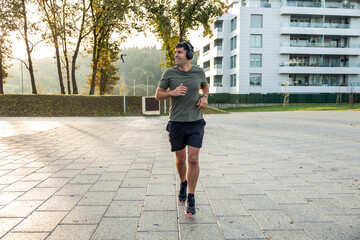 Latin man running smiling with headphones in city park