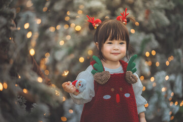 Cute little girl in reindeer outfit smiling happily with Christmas lights glowing in the background, festive holiday atmosphere, warm and joyful Christmas moment