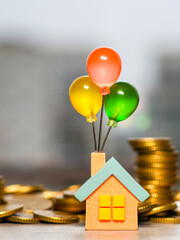 Colorful balloon house figurine surrounded by gold coins symbolizing dreams of owning a home