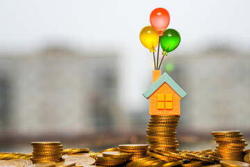 Mini house with colorful balloons standing on stacked gold coins symbolizing dreams of owning a home
