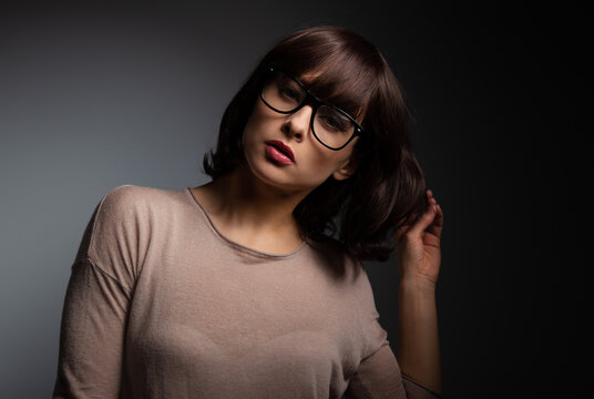 Serious thinking female model with black short hair posing in fashion eye glasses on dark shadow background with copy space. Closeup fashion low key art style portrait