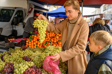 Woman shopping at a farmers market, selecting fresh seasonal vegetables and fruits. Natural light, vibrant produce, sustainable lifestyle and healthy home cooking concept.
