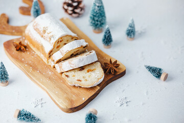 Sliced festive bread with powdered sugar and spices on a wooden board with miniature trees