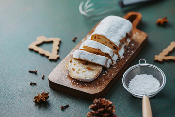 Sliced fruitcake dusted with powdered sugar on wooden board with spices and cookie cutters