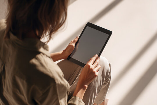 Woman using a tablet in warm sunlight — relaxed indoor lifestyle scene with blank screen for mockup, digital reading, remote work, and cozy leisure.