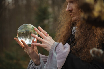 Man with long hair gazes at crystal ball in a forest outdoors