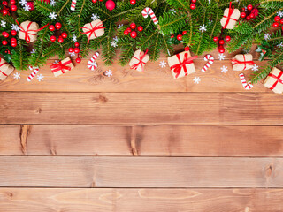 Christmas holiday border with gifts, candy canes, and fir branches on wooden background