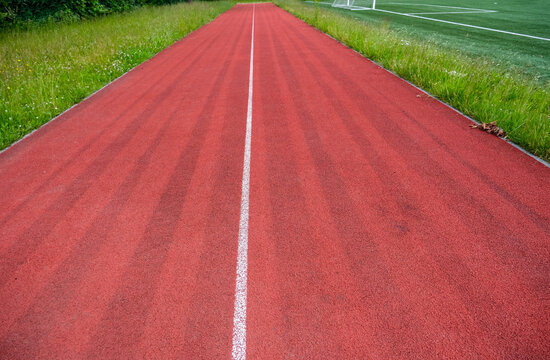Weiter Blick auf eine viel genutzte Tartan Laufbahn f&uuml;r Leichtathletik neben einem Fu&szlig;ballplatz mit Kunstrasen in einer Sportanlage, viel Copy Space