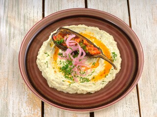 A creative and carefully prepared dish of baba ghanoush is served. Eggplant, pickled onions, and fresh parsley decorate the tasty plate on a rustic wooden table in the kitchen