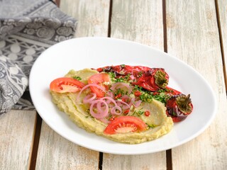 Delicious home made pate is served on a white plate. Roasted red peppers, tomato slices, and onion rings top this Mediterranean food. Served on a Summer afternoon on a rustic wooden table