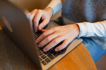 Closeup of hands typing on a laptop keyboard in a cozy cafe environment, representing concepts of remote work, productivity, digital communication, creative workflow and modern workspace lifestyle.