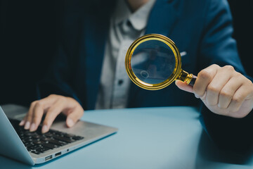 Business person holding magnifying glass near laptop, concept of analysis and research, investigation and inspection, focus on magnifier lens with blurred background