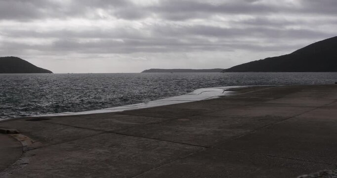 Empty beach at seaside at early autumn, Boka bay, Adriatic sea, Montenegro, Mediterranean, waves flushing concrete beach on cloudy day