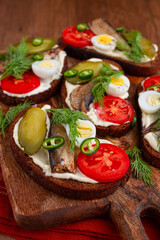 open sandwiches with sprats, vegetables and herbs, on a wooden board, breakfast, snack,