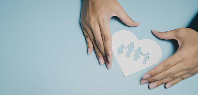 Family protection concept with hands surrounding paper heart cutout showing family figures, symbolizing care, love, and in soft blue background