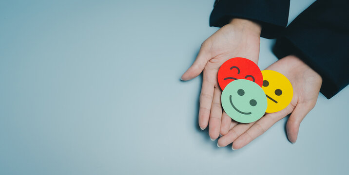 Colorful paper smiley face held in hands, representing different emotions and feelings with red, green, and yellow colors on blue background, conveying mood and expression