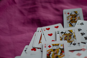 Scattered playing cards on a purple surface, casually arranged, overlapping, creating a chaotic and playful atmosphere.