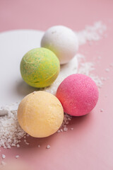 Bath bombs with scattered sea salt on a pink background. At-home spa treatments for relaxation and restoration. Fizzing bath bombs for aromatherapy and skin care. Cosmetic product