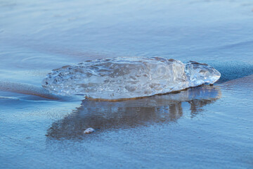 Ice block washed ashore on wet beach sand with soft reflection © Kersti Lindström