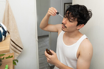 Man in the bathroom applying skincare with a dropper to his face as part of his morning facial care routine. A concept of wellness and self care at home