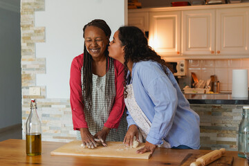 Happy african daughter kissing her mother while preparing Christmas bread at home - Holiday, festive and family lifestyle concept
