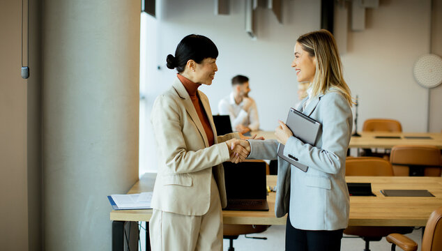 Two businesswomen shaking hands in a modern office setting during a meeting