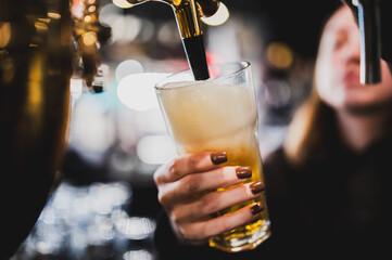 Close-up of bartender pouring a draft beer from a tap into a pint glass at a pub or bar, shallow depth of field, warm atmosphere, copy space available