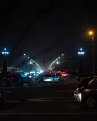 Fototapeta premium Nighttime city bridge with trams and cars moving through fog, illuminated by bright streetlights and overhead wires. The scene captures a moody urban atmosphere with soft light reflections.