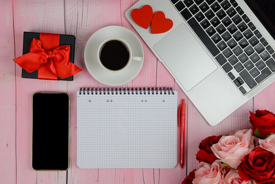 Laptop computer and an open heart-shaped gift box on a dark wooden table against a background of lights. Online shopping and chatting, virtual Valentine's Day, love in time COVID-19 concept.