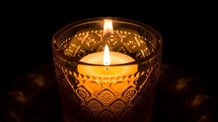 Warm candlelight glows in decorative glass holder against a dark background