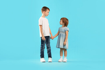 Full-length portrait of little boy and girl on light blue background