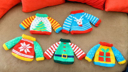 Colorful miniature knitted Christmas sweaters featuring festive patterns such as a snowflake, reindeer, gift box, Christmas tree, and an elf outfit