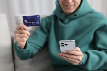 Young man making online payment with phone and credit card indoors, closeup