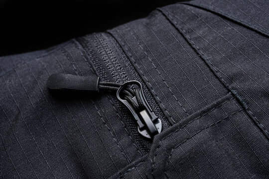 Close up of black zipper slider on men cargo pants. Macro detail of tactical clothing pocket made of durable ripstop fabric texture. Photo