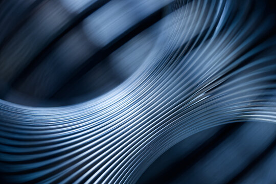 Abstract industrial metal background with curved steel lines on dark blue. Macro texture of shiny silver spring coil for hardware manufacturing presentation. Photo