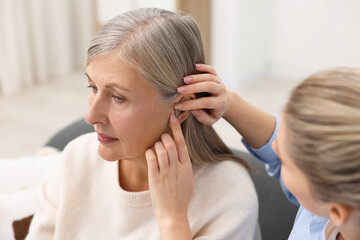 Woman putting hearing aid into her mother's ear at home, closeup