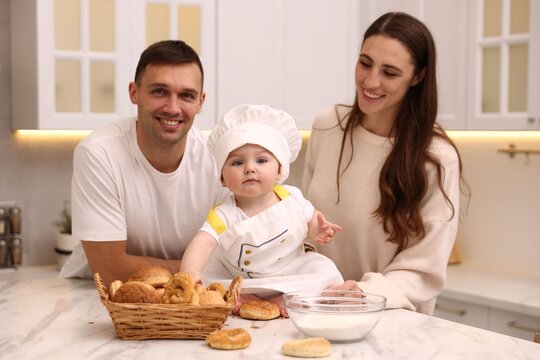 Parents and their cute baby wearing chef uniform at table in kitchen