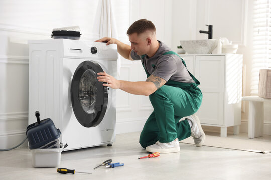 Repairman in uniform examining broken washing machine at home