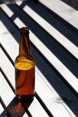 A chilled amber glass beer bottle filled with lager standing beside shadow lines on a wooden bench
